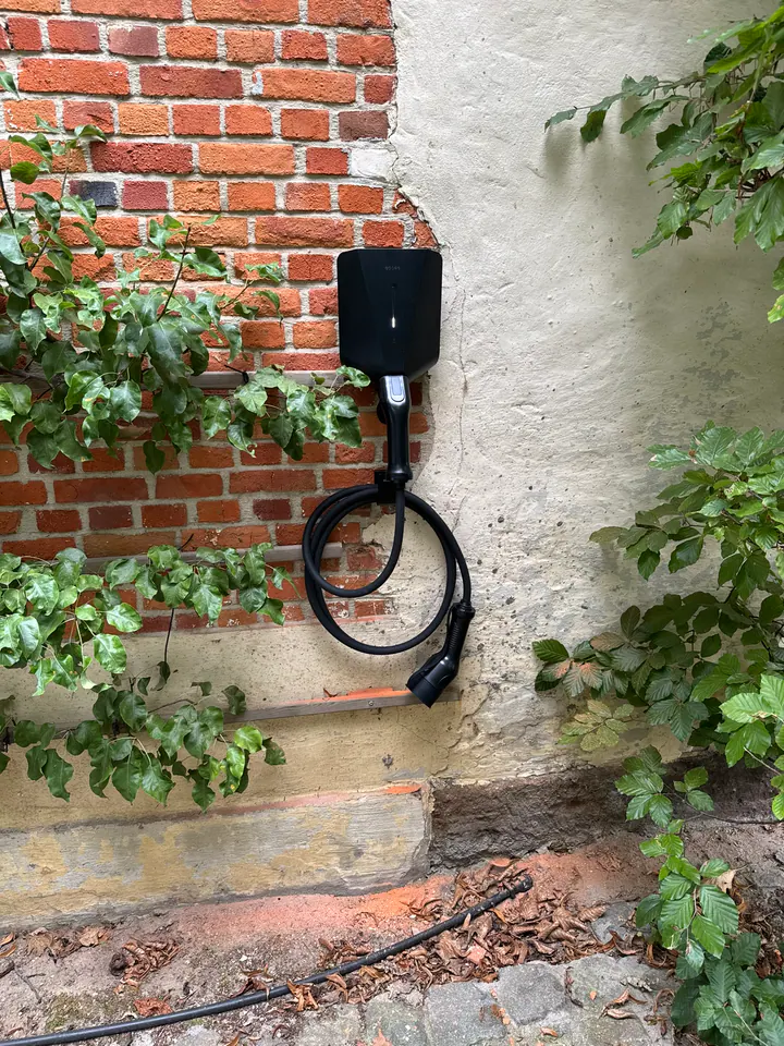 Zwarte Easee-lader met opgerolde laadkabel aan een tuinmuur tussen het groen, geplaatst door Laadnatie.