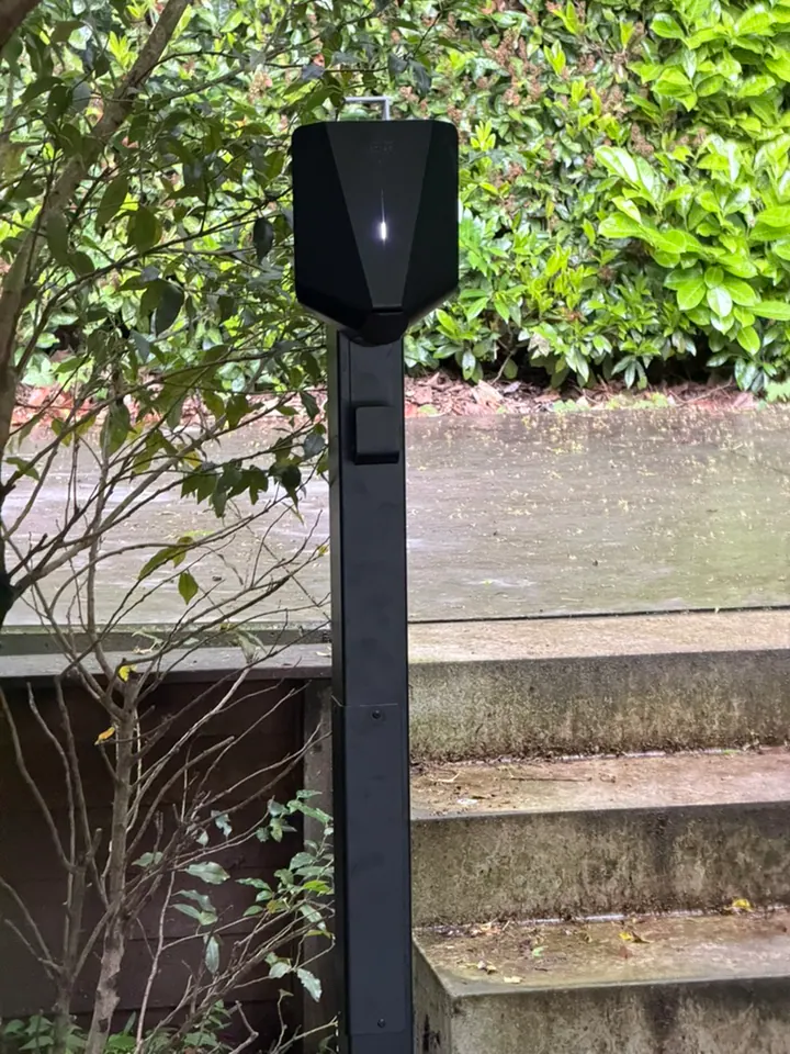 Zwarte Easee-lader op een montagepaal in een groene tuin, geplaatst door Laadnatie.