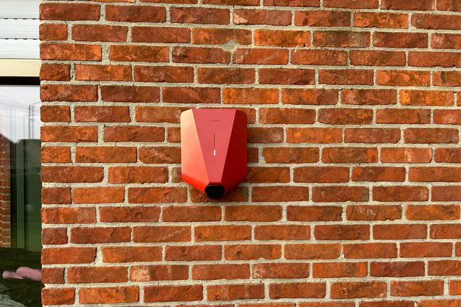 Rode Easee-lader aan een rode bakstenen buitenmuur, geplaatst door Laadnatie.