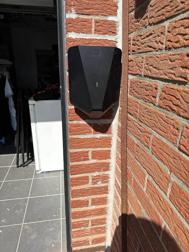 Zwarte Easee-lader aan een zonnige rode bakstenen garagemuur, geplaatst door Laadnatie.