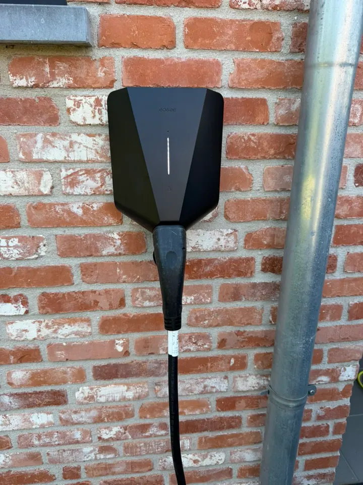 Zwarte Easee-lader met ingeplugde laadkabel aan een bakstenen muur, geplaatst door Laadnatie.