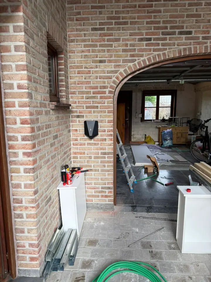Zwarte Easee-lader aan een bakstenen muur tijdens een renovatie, geplaatst door Laadnatie.