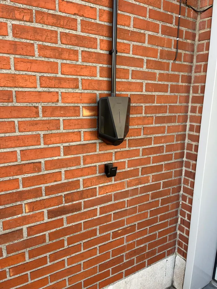 Zwarte Easee-lader met zwarte kabelgoot aan een rode bakstenen muur, geplaatst door Laadnatie.