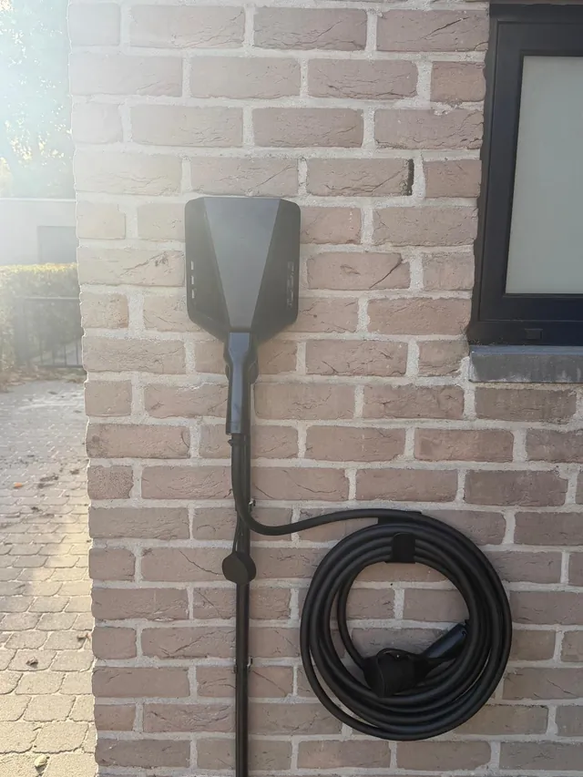 Zwarte Easee-lader met aangesloten laadkabel en een opgerolde kabel op een houder aan een bakstenen gevel, geplaatst door Laadnatie.